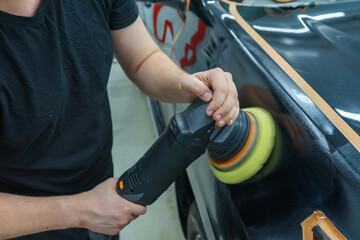 Taking care of the car's appearance. The master polishes the front fender of a black car.