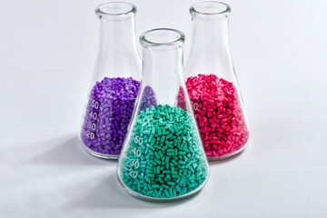 Red, purple and turquoise masterbatch granules in Erlenmeyer flask isolated on white background,...
