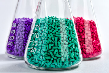 Red, purple and turquoise masterbatch granules in Erlenmeyer flask isolated on white background,...