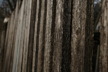 Obraz premium A close-up of a weathered wooden fence showcases the rough texture and aged wood grain. The planks are vertically aligned, with gaps creating depth and contrast between light and shadow.