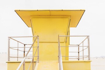 Bright yellow lifeguard tower overlooking a serene beach at midday