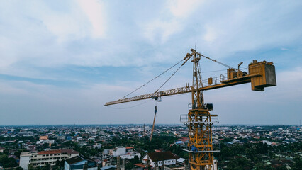Naklejka premium Tower crane at a construction site against a cloudy sky, captured from a drone