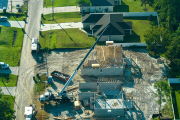 Aerial view of lifting crane and builders working on unfinished residential house with wooden roof...