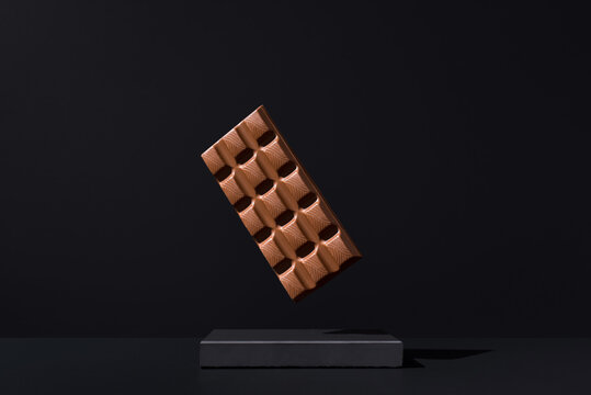 Dark chocolate bar levitating on black background