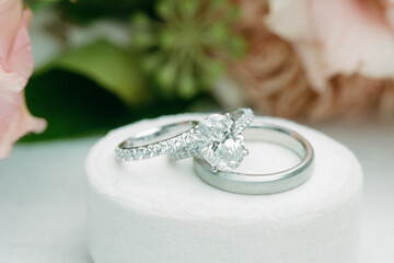 Elegant wedding rings displayed on a soft white cushion amid beautiful floral arrangement