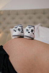 Cute baby booties on a pregnant belly in a cozy bedroom setting during a relaxing moment at home