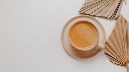 Beige ceramic cup of coffee closeup with palm leaves on white wooden background with copy space for design