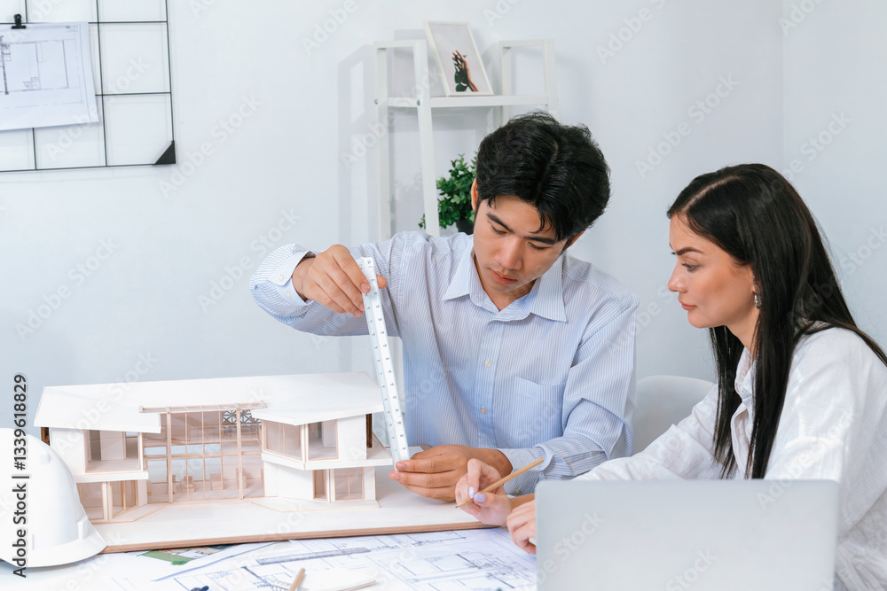 Poster professional male asian architect using ruler to measure house model length while young beautiful ca