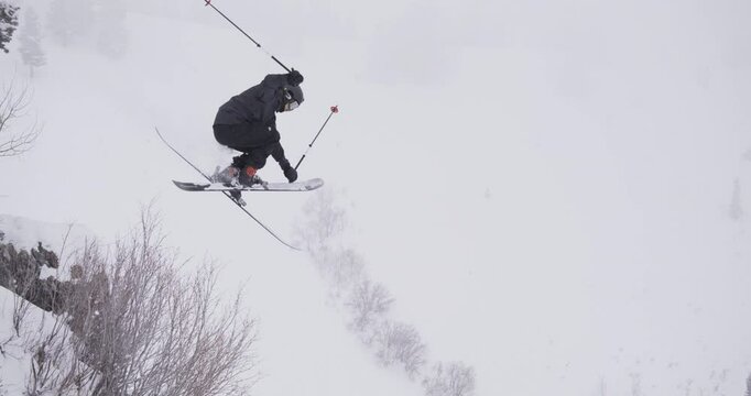 Extreme ski athlete jumping off rocky ledge and speeding off into snowy field