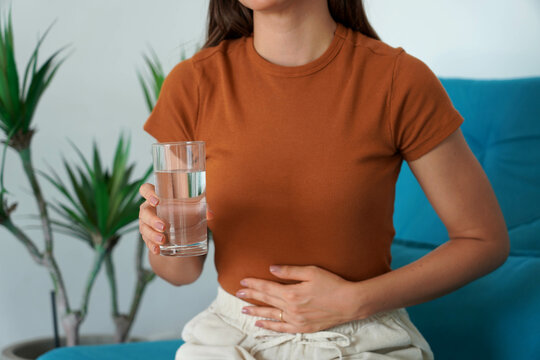 Eating Disorder. Unrecognizable girl suffering from abdominal pain holds a glass of water in her hand. Unregulated Intestine.