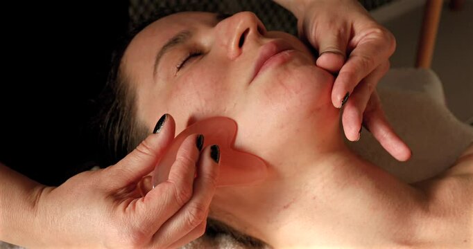 Young woman receiving facial massage with gua sha tool in beauty salon
