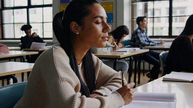 A group of students concentrate on their examinations in a well-lit classroom. They write diligently in their notebooks while the atmosphere remains quiet and focused