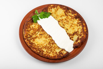 Golden brown potato pancake with sour cream and fresh parsley on a rustic clay plate. Traditional Eastern European dish, crispy texture and exquisite homemade taste, homemade dish