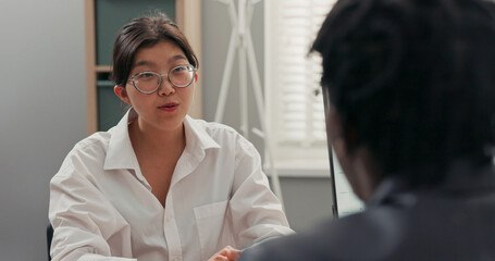 head of company, dark-skinned in suit, talks to candidate for position of office secretary girl with Asian features jokes with man they laugh job interview shaking hands to thank for meeting, goodbye