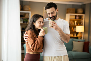 The couple exudes joy as they stand close, sipping coffee in a cozy setting that reflects their love and comfort.