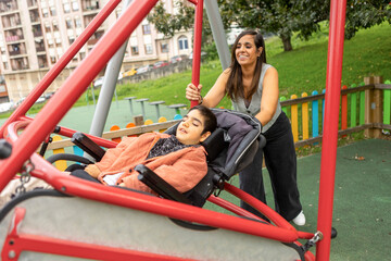 Mother pushes son with cerebral palsy on adaptive swing in park