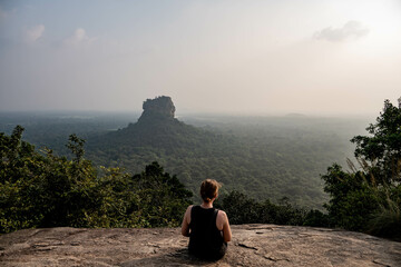 woman sitting on pidurangala rock with a view on lion rock, sigiriya, sri lanka