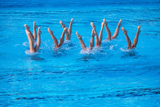 Artistic swimmers team performing synchronized legs choreographed movement in the swimming pool