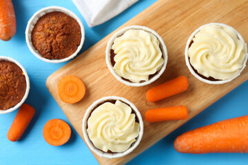 Tasty carrot muffins with fresh vegetables on light blue wooden table, flat lay