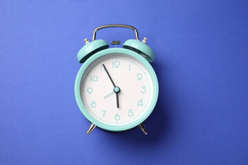 One turquoise alarm clock on blue background, top view