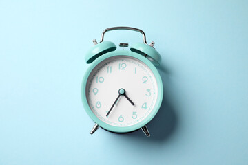 Turquoise alarm clock on light blue background, top view