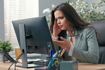 Beautiful busy businesswoman sits at desk in front of computer in office, has technical problems...