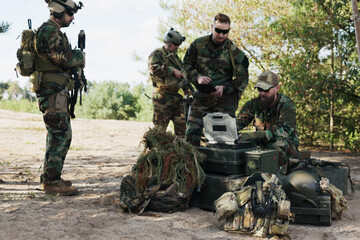 Army troops in camouflage uniforms and helmets prepare for battle at the training ground, holding a...