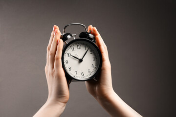 Woman with black alarm clock on grey background, closeup