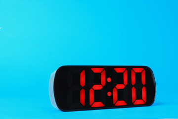 Digital alarm clock showing 12:20 o'clock on light blue background