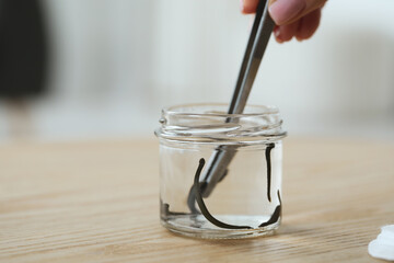 Woman taking leech from jar with tweezers on wooden table, closeup