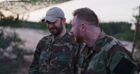 Fototapeta premium Soldiers in camouflage clothing gather around a campfire in the evening, frying sausages for supper, joking, laughing, and relaxing after a long day of service and field exercises.