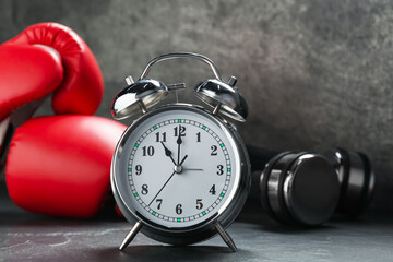 Alarm clock, boxing gloves and dumbbells on grey background