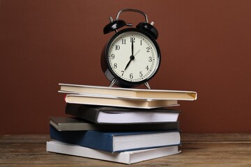 Naklejka premium Time for knowledge. Alarm clock and books on wooden table
