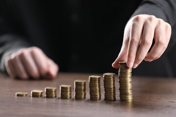 Man putting coins onto stacks of ones at wooden table, closeup