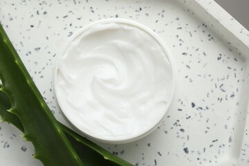Moisturizing cream with extract of aloe vera in jar and cut leaves on white plate, top view