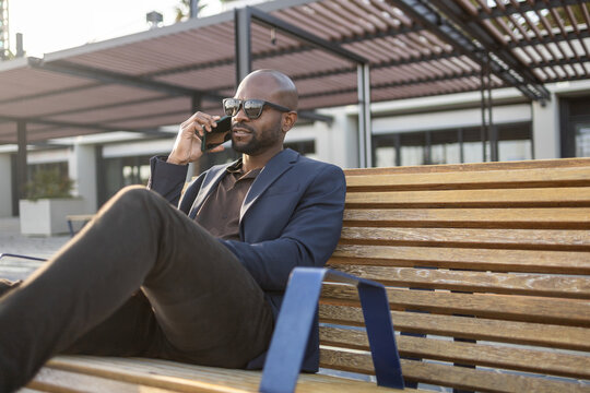 Business cuban man taking a phone call on a bench wearing sunglasses