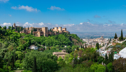Fototapeta premium Granada, Spain - the majestic Alhambra palace overlooking the lush green hills and historic Albaicín district under a clear blue sky