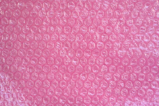 Close-up of the texture of pink bubble wrap as a background. Transparent air-filled pockets create a structured, homogeneous pattern with a shiny, reflective surface. The bright pink colour accentua - Powered by Adobe