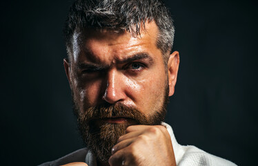 Karate man preparing for competition. Strong muscular fighter ready for karate training. Closeup portrait of bearded athlete practicing aikido or taekwondo. Karate man in kimono in fighting position.