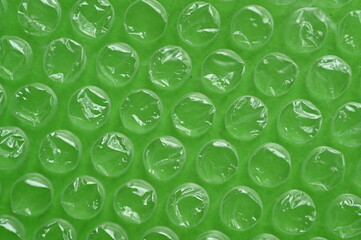 Close-up of the texture of green bubble wrap as a background. Transparent air-filled pockets create a structured, homogeneous pattern with a shiny, reflective surface. The bright green colour accentua