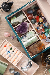Box with beautiful gemstones and jeweler's tools on wooden table, flat lay