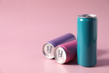 Colorful aluminium cans of beverage on pink background, space for text
