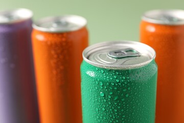 Colorful aluminium cans of beverage on pale green background, closeup