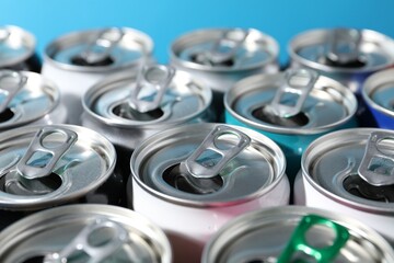 Many aluminium cans of beverage on light blue background, closeup