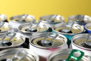 Many aluminium cans of beverage on yellow background, closeup