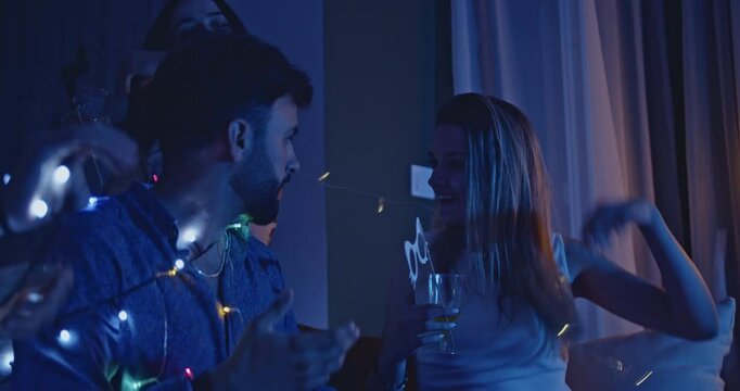 Friends enjoying drinks and having fun at a birthday party at home. They are wearing party favors and festive string lights and smiling.