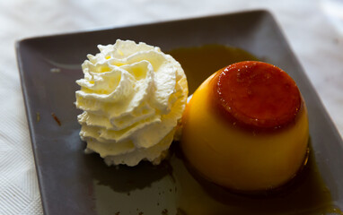Image of tasty dessert cream flan served with butter cream at black plate