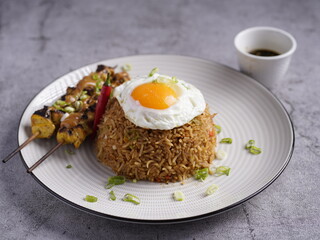 Nasi goreng with fried egg, chicken satay skewers, and soy dipping sauce, served on a plate with garnish.
