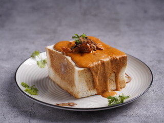 Bread bowl filled with creamy curry, topped with meat and garnished with herbs, served on a plate in a rich and comforting style.