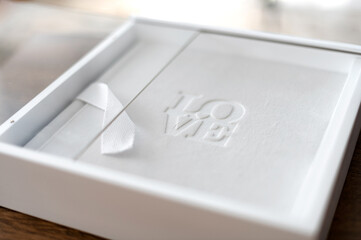 Elegant white gift box with embossed love design displayed on a wooden table, showcasing a thoughtful present for special occasions. In the box is a photobook